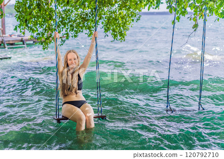 Beautiful female tourist relaxing on a swing in Laguna Bacalar in Mexico during kayak trip. Female tourist swinging over Lake Bacalar with feet in the water. Quintana Roo, Mexico travel, relaxation 120792710