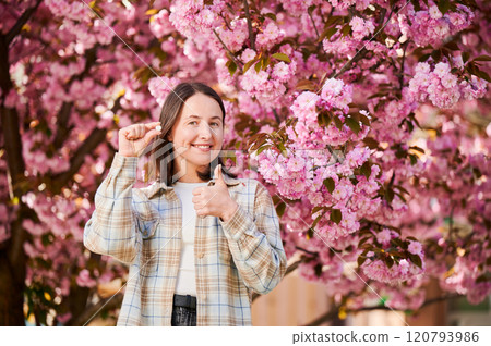 Woman allergic suffering from seasonal allergy at spring. Young happy woman showing allergy pill, giving thumbs up, posing in blossoming garden at springtime. Antihistamine medication concept 120793986