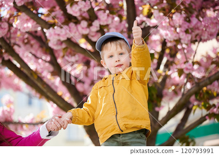 Young boy allergic enjoying after treatment from seasonal allergy at spring. Portrait of happy guy smiling, showing thumbs up gesture in front of blooming tree at springtime. Spring allergy concept. 120793991