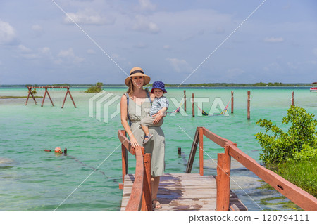 Mother with his toddler son exploring wooden pier over the turquoise waters of Bacalar Lake, Mexico. Peaceful tropical travel destination concept Mother with his toddler son exploring wooden pier over the turquoise waters of Bacalar Lake, Mexico. Peaceful tropical travel destination concept 120794111