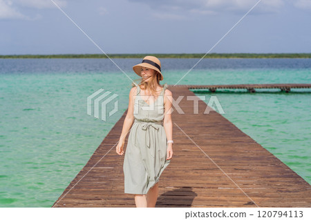 Female tourist in a turquoise dress standing on a wooden pier over the turquoise waters of Bacalar Lake, Mexico. Peaceful tropical travel destination concept Female tourist in a turquoise dress standing on a wooden pier over the turquoise waters of Bacalar Lake, Mexico. Peaceful tropical travel destination concept 120794113