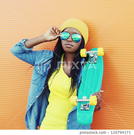 Portrait of modern young african woman model posing in colorful clothes, yellow hat with skateboard Portrait of modern young african woman model posing in colorful clothes, yellow hat with skateboard 120794171