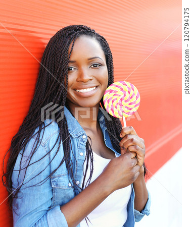 Happy smiling young african woman with sweet lollipop over red background 120794175