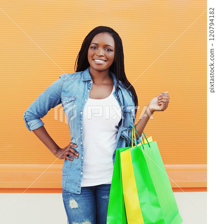 Portrait beautiful smiling young african woman with shopping bags in city on colorful background 120794182