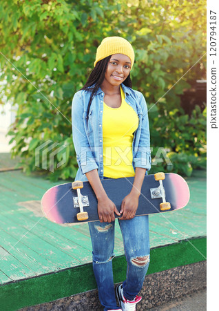 Portrait of happy smiling young african woman model posing with skateboard in the city 120794187