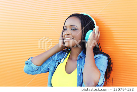 Pretty smiling african woman with headphones enjoying listens to music over orange background 120794188
