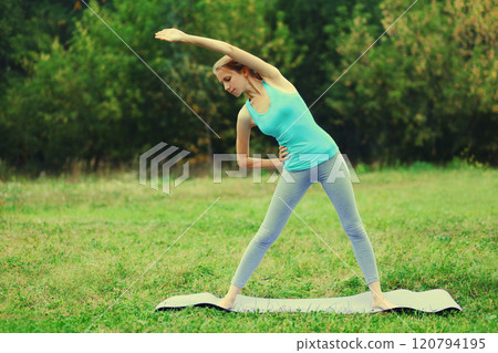 Fitness woman doing yoga exercises on a mat on the grass in summer park 120794195