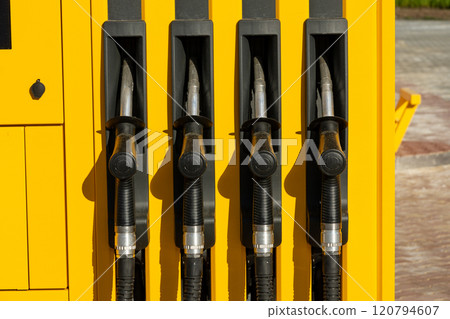 Four pump nozzles are lined up at a gasoline station, showcasing a bright yellow design against a clear daytime backdrop. The area is well-lit and inviting Four pump nozzles are lined up at a gasoline station, showcasing a bright yellow design against a clear daytime backdrop. The area is well-lit and inviting 120794607