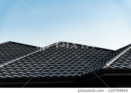 The dark tiled roof features a unique pattern and slopes elegantly, contrasting beautifully with the bright blue sky above a suburban home during daylight hours The dark tiled roof features a unique pattern and slopes elegantly, contrasting beautifully with the bright blue sky above a suburban home during daylight hours 120794640