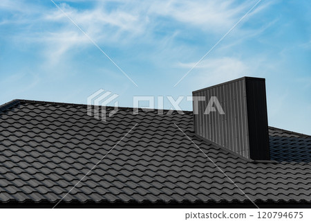Roof of house is covered with black metal modern roofing material against the sky. Corrugated metal roof and metal roofing 120794675