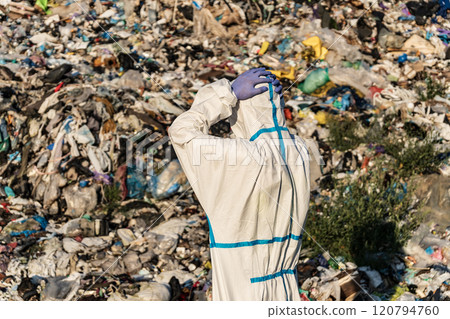 Man with bacteriological protective holding his hands behind his head. Pile of domestic garbage in landfill dump site. Global environmental issue of waste disposal Man with bacteriological protective holding his hands behind his head. Pile of domestic garbage in landfill dump site. Global environmental issue of waste disposal 120794760