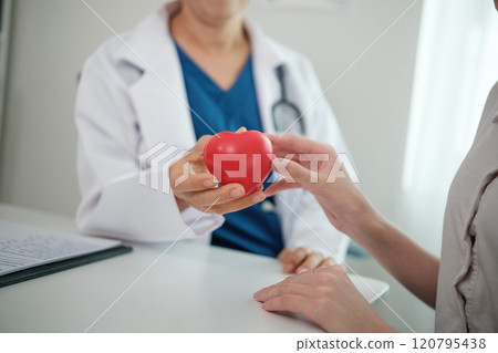 A doctor is holding a red heart in front of a patient 120795438