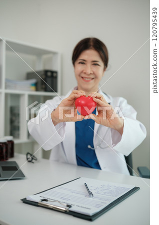 A woman in a white coat holding a red heart 120795439