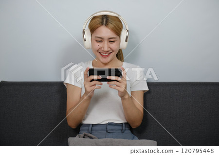 A woman is sitting on a couch and playing a game on her phone A woman is sitting on a couch and playing a game on her phone 120795448