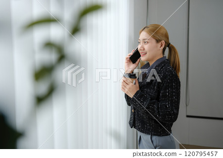 A woman is talking on her cell phone while holding a cup of coffee A woman is talking on her cell phone while holding a cup of coffee 120795457
