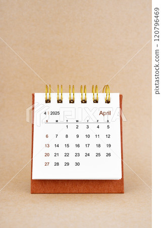 April 2025 white desk calendar on brown background. 120796469