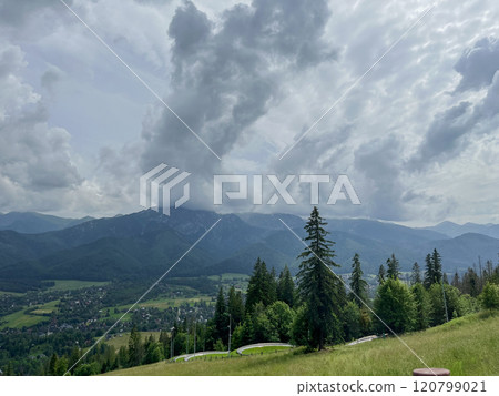 landscape Photo of mountains covered with green forests and grass, and shrouded in white clouds. You can see the town in the distance. tatras, poland, 120799021