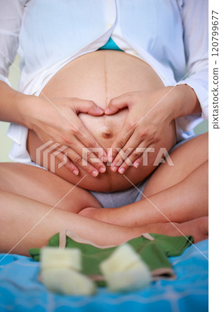 pregnant woman forms heart shape with her hands on her belly, expressing joy 120799677