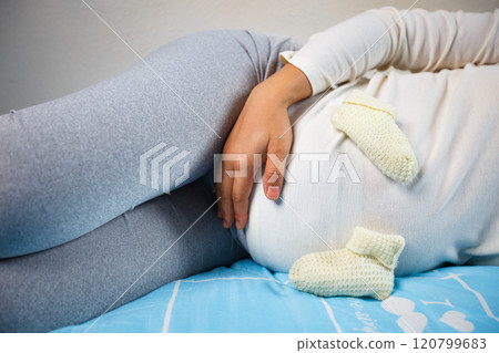 Expecting mother relaxing with baby booties on her belly, joyful anticipation Expecting mother relaxing with baby booties on her belly, joyful anticipation 120799683
