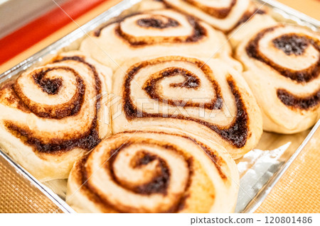 Just out of the oven, cinnamon rolls cool on a silicone baking mat, their icing glistening under the kitchen lights. 120801486