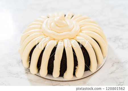 With precision, the Chocolate Bundt Cake is carefully removed from the pan - adorned with luscious cream cheese frosting, creating a delectable treat that is sure to delight. 120801562