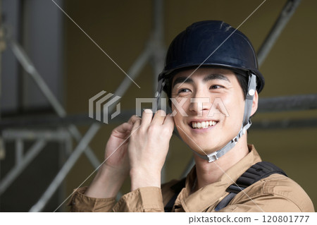 A man wearing a helmet with a safety belt at the work site A man wearing a helmet with a safety belt at the work site 120801777