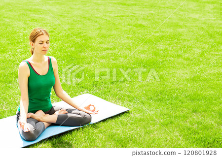 A woman practices yoga outdoors on the grass. Copy space 120801928