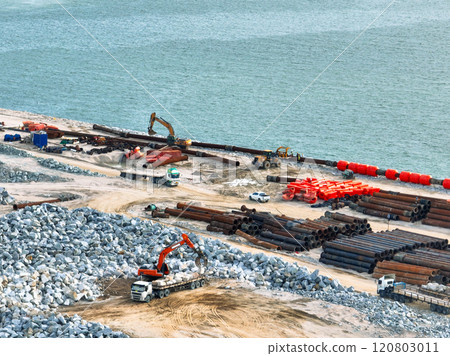 Construction progress on shipping port terminal through land reclamation. Global trade development, infrastructure engineering, and marine environmental sustainability efforts. Maritime infrastructure Construction progress on shipping port terminal through land reclamation. Global trade development, infrastructure engineering, and marine environmental sustainability efforts. Maritime infrastructure 120803011