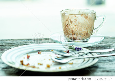 Empty coffee cup with stained interior and empty dessert plate with crumbs and utensils, placed on rustic wooden table near window light Empty coffee cup with stained interior and empty dessert plate with crumbs and utensils, placed on rustic wooden table near window light 120804092
