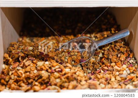 A wooden box containing a dry herbal tea blend and a metal scoop 120804583