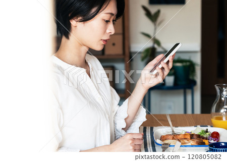 Woman eating breakfast while looking at smartphone 120805082