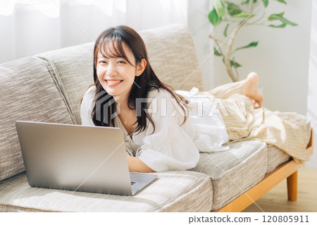 A woman using a computer while lying on the sofa 120805911