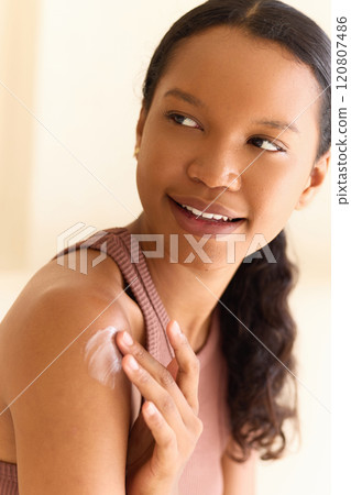 Young Woman Applying Moisturizing Cream to Her Shoulder with a Smile Young Woman Applying Moisturizing Cream to Her Shoulder with a Smile 120807486