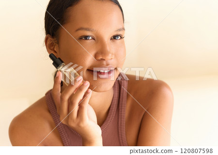 Young Woman Holding Skincare Serum Bottle With a Gentle Smile Young Woman Holding Skincare Serum Bottle With a Gentle Smile 120807598