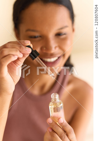 Smiling Woman Applying Nourishing Face Serum With Dropper in Bright Light Smiling Woman Applying Nourishing Face Serum With Dropper in Bright Light 120807604