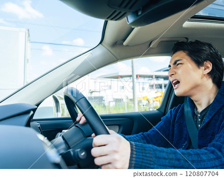 A male driver driving a car while feeling irritated A male driver driving a car while feeling irritated 120807704