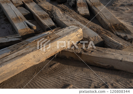 Close-up of weathered wooden beams on sandy beach landscape at sunset 120808344