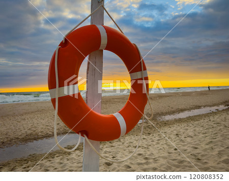 Orange lifebuoy on sandy beach during beautiful sunset 120808352
