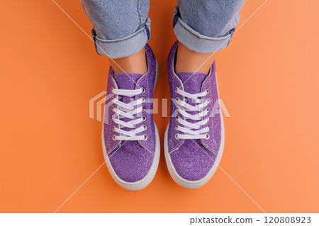 High-top sneakers on legs. Shiny details. Glitter sporty shoes, white soles. Sparkly purple sneakers, orange background. Sparkling pair of casual sneaker shoes. Glittery Footwear. Glamour urban style 120808923