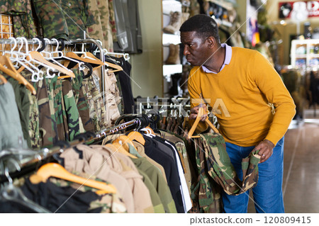 Male shopper chooses camouflage uniform at army store Male shopper chooses camouflage uniform at army store 120809415