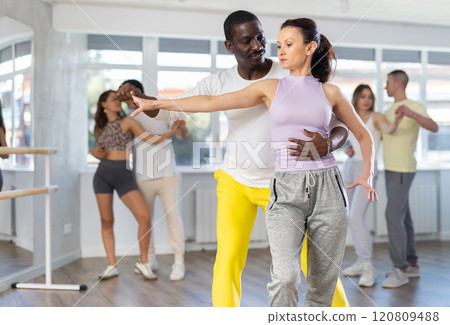 Positive African american man and european woman dancing and training movements Latin dance bachata during group class in choreography studio Positive African american man and european woman dancing and training movements Latin dance bachata during group class in choreography studio 120809488