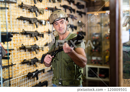 Man in armor vest selecting machine gun in air weapon shop 120809501