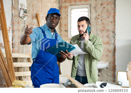 Worker and owner building discuss construction plan inside building under construction Worker and owner building discuss construction plan inside building under construction 120809533