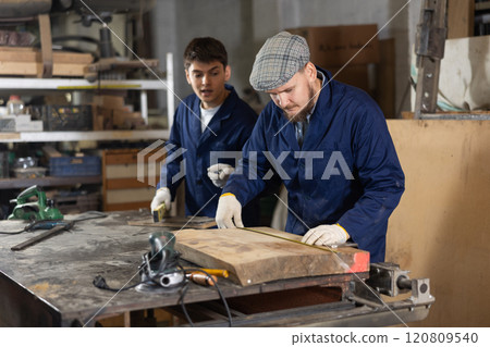 Carpenter measures the length of board with tape measure. Foreman prompts him 120809540