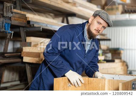 Male furniture assembler assembles wooden table at furniture factory Male furniture assembler assembles wooden table at furniture factory 120809542