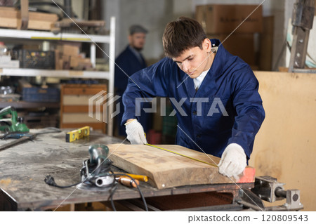 Young guy measuring wooden board with tape measure 120809543