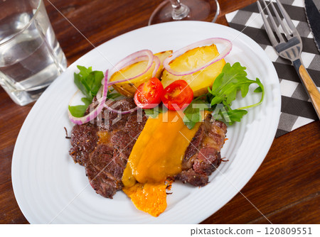 Well-done beef steak with baked potatoes and cheese served at plate Well-done beef steak with baked potatoes and cheese served at plate 120809551