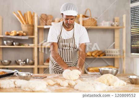 Adult male baker kneading dough on table Adult male baker kneading dough on table 120809552