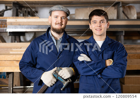 Portrait of two carpenters in uniform in the interior of furniture factory Portrait of two carpenters in uniform in the interior of furniture factory 120809554