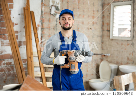 Young bearded builder holding pneumatic jackhammer in building under renovation Young bearded builder holding pneumatic jackhammer in building under renovation 120809648